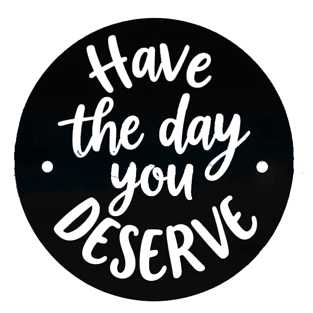 Round black decal with white and black script lettering that reads “Have the day you deserve,” with two small white mounting dots on the sides.